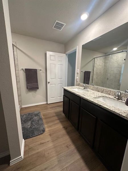 Full bath featuring double vanity, dark wood-style flooring, a stall shower, and a textured wall