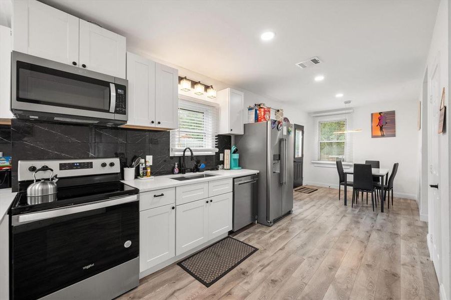 Kitchen featuring stainless steel appliances, light countertops, white cabinetry, light wood-type flooring, and decorative backsplash Kitchen featuring stainless steel appliances, light countertops, white cabinetry, light wood-type flooring, and decorative backsplash