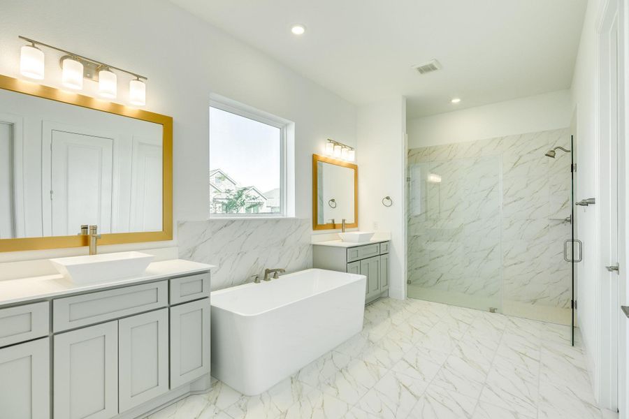 Stunning primary bath featuring exquisite tile flooring and elegant gold trim accents. This luxurious space includes sophisticated mirrors paired with modern lighting, a tranquil soaking tub positioned beneath a window for soft natural light, and an expansive, oversized glass walk-in shower.