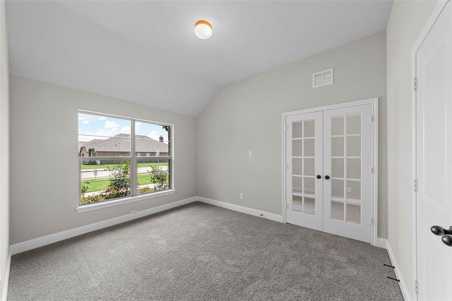 Spare room featuring vaulted ceiling, french doors, and carpet floors