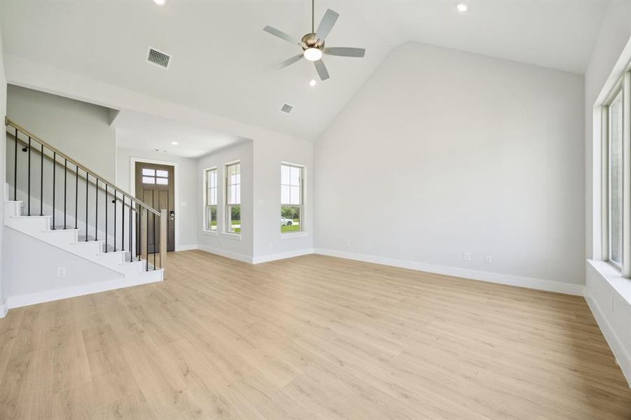 Unfurnished living room with stairway, high vaulted ceiling, light wood-style floors, recessed lighting, and ceiling fan