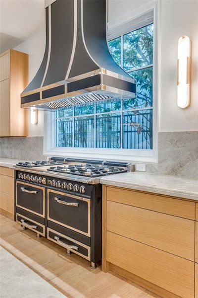 Kitchen with backsplash, range with two ovens, light wood-type flooring, light brown cabinetry, and island range hood