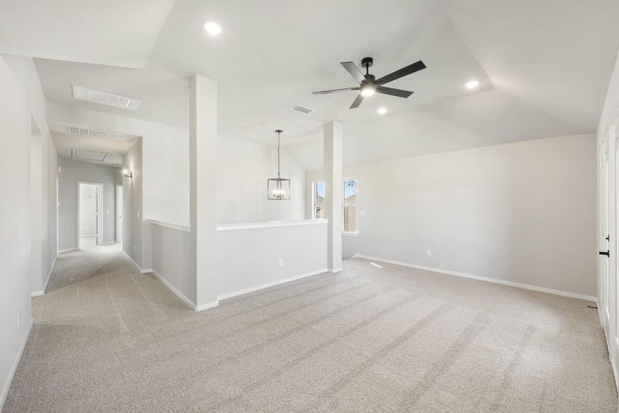 Open living area with vaulted ceiling, ceiling fan, pendant light, and neutral carpet flooring