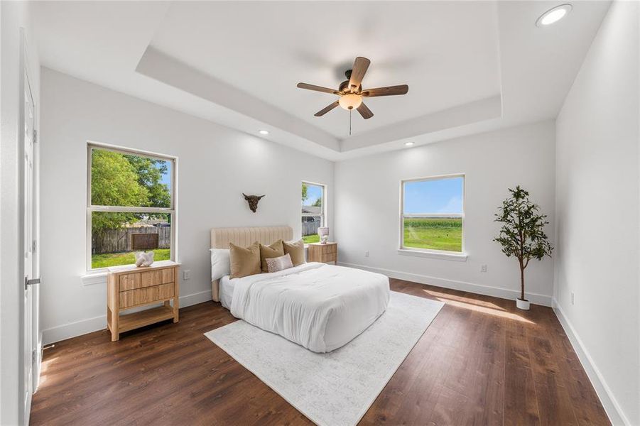 Spacious bedroom featuring a tray ceiling with recessed lighting, wood-finish flooring, and multiple windows