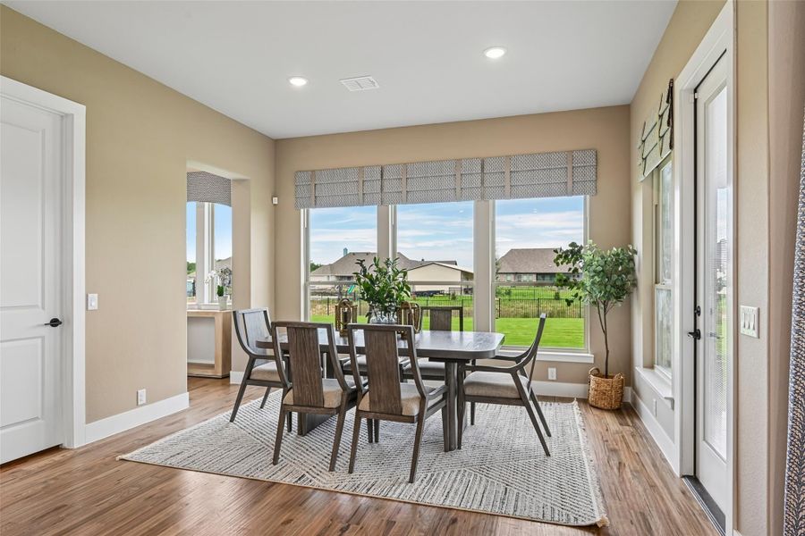 Dining room with dark wood table and chairs, hardwood floors, and large windows overlooking a backyard Dining room with dark wood table and chairs, hardwood floors, and large windows overlooking a backyard