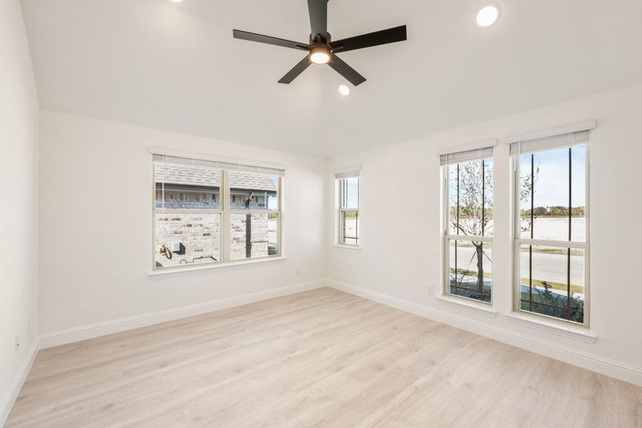 Empty bedroom with light wood floors, white walls, ceiling fan, and multiple windows