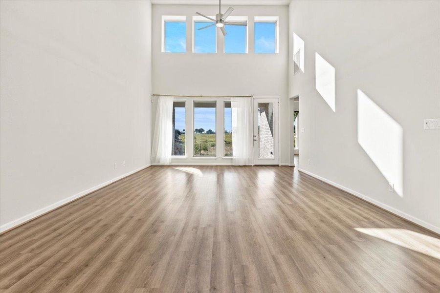 Unfurnished living room featuring plenty of natural light, a ceiling fan, wood finished floors, and a towering ceiling Unfurnished living room featuring plenty of natural light, a ceiling fan, wood finished floors, and a towering ceiling