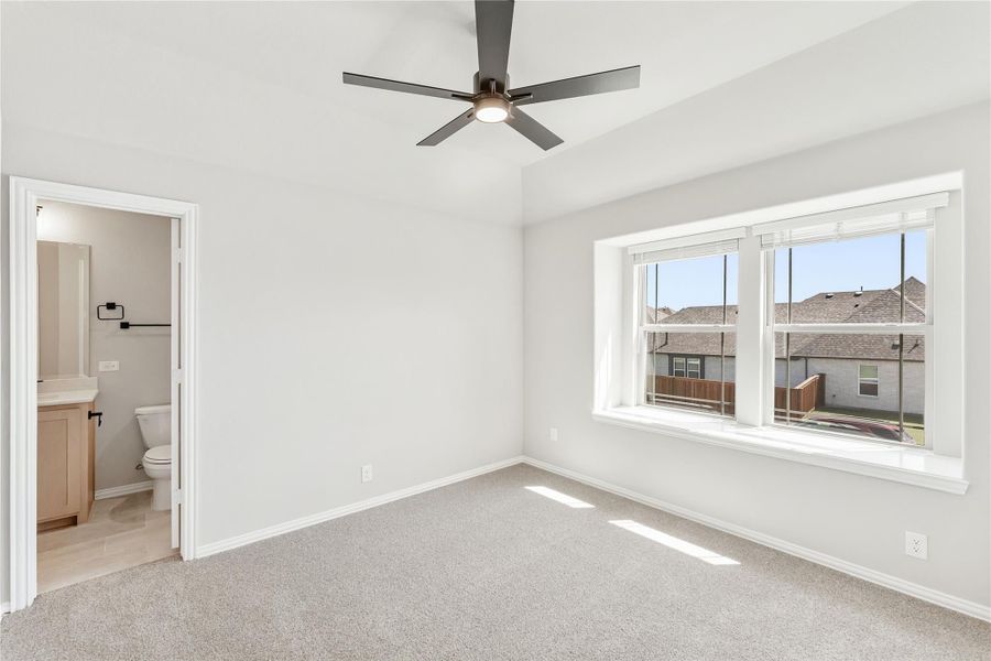 Empty bedroom with carpet, ceiling fan, large window, and ensuite bathroom doorway