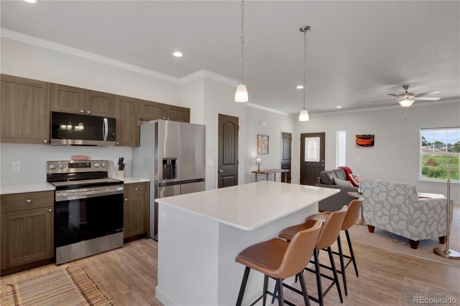Kitchen featuring appliances with stainless steel finishes, light wood-style flooring, crown molding, a kitchen breakfast bar, and a center island