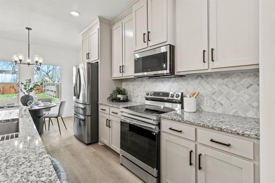 Kitchen with light stone counters, light wood finished floors, an inviting chandelier, appliances with stainless steel finishes, and backsplash