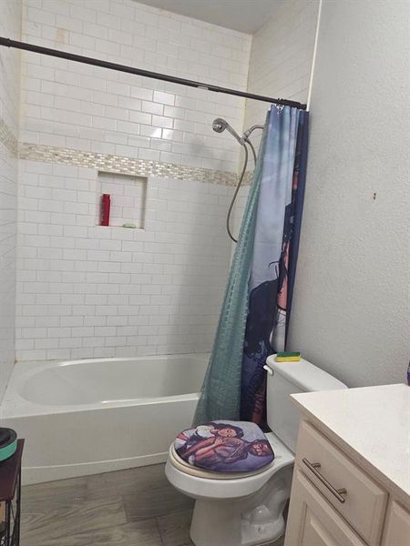 Full bathroom featuring vanity, shower / bath combination with curtain, a textured wall, and dark wood-type flooring