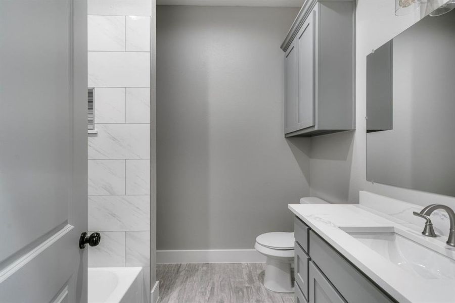 Full bathroom with wood-type flooring, vanity, tiled shower / bath, and toilet