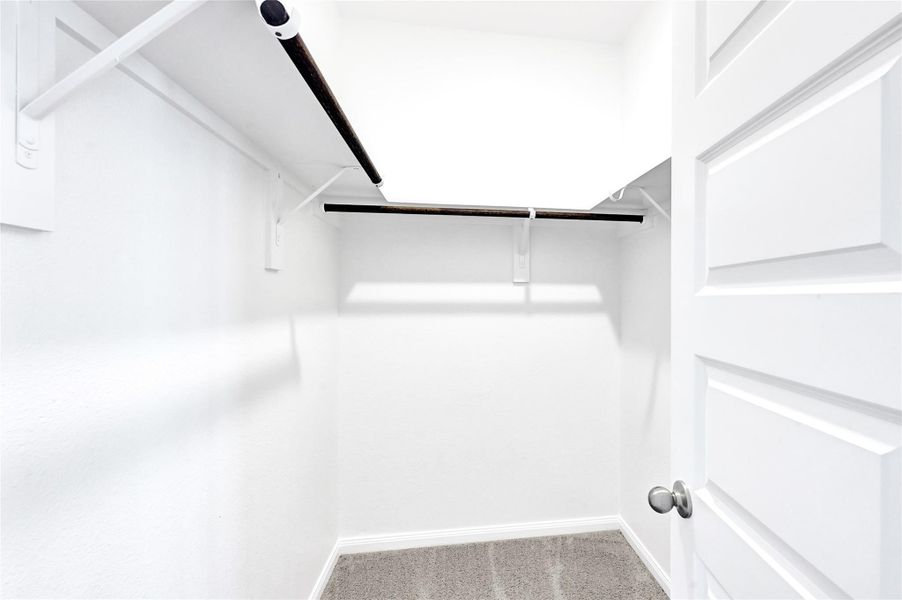 This is a spacious walk-in closet with white walls, carpeted flooring, and multiple hanging rods for ample storage.Please note: The image is not the actual home; it is a home with the same floor plan in the neighborhood.