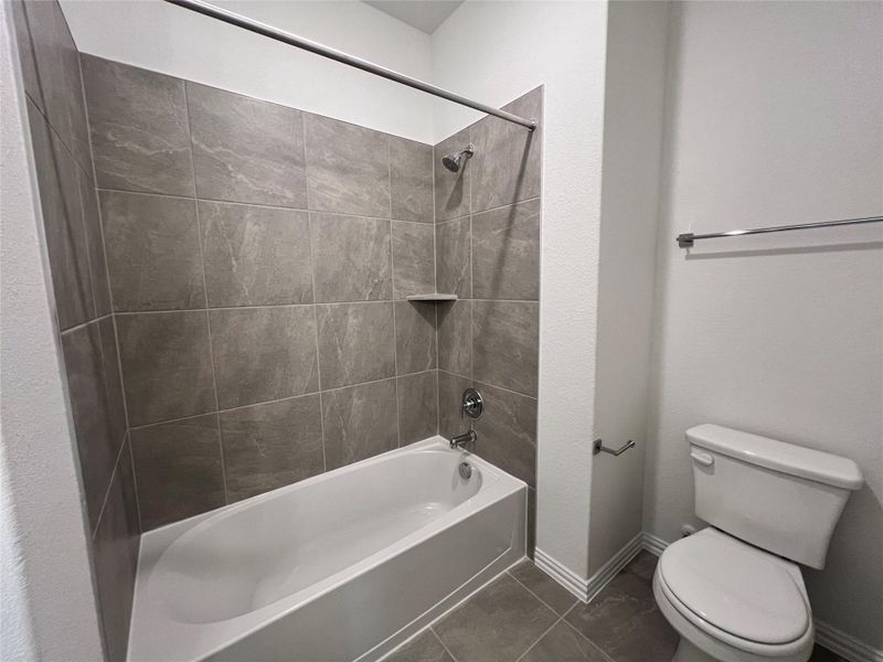 Bathroom featuring tub / shower combination and dark tile patterned flooring