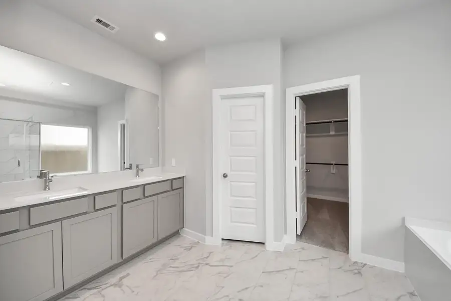 Escape to a spa-like oasis in this primary bathroom. Enjoy a walk-in shower with tile surround, a separate garden tub with custom detailing, and an elegant vanity featuring light countertops, modern hardware, and beautiful recessed lights. Experience luxury and relaxation in every detail. Sample photo of completed home with similar floor plan. Actual colors and selections may vary.