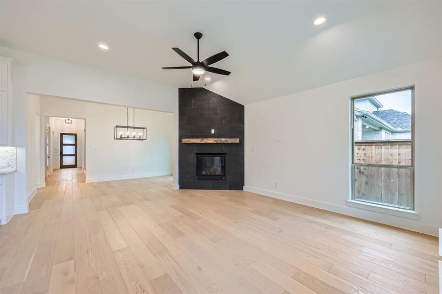 Unfurnished living room with light wood-type flooring, lofted ceiling, ceiling fan, and a fireplace