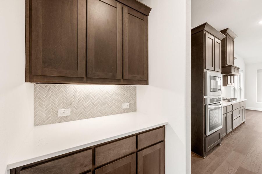 Kitchen with dark brown cabinets, herringbone tile backsplash, white countertops, and stainless steel appliances on hardwood floors