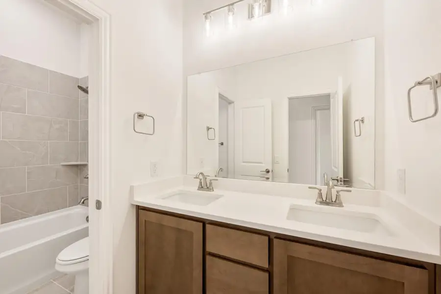 Bathroom with double sink vanity, wood cabinets, large mirror, and tiled tub-shower combo Bathroom with double sink vanity, wood cabinets, large mirror, and tiled tub-shower combo