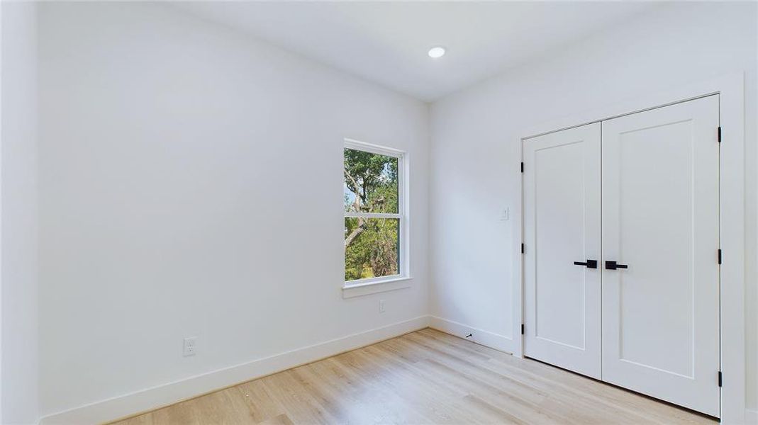 The spacious secondary bedroom features wood-look LVP flooring, recessed lighting, and a large window that fills the room with natural light.