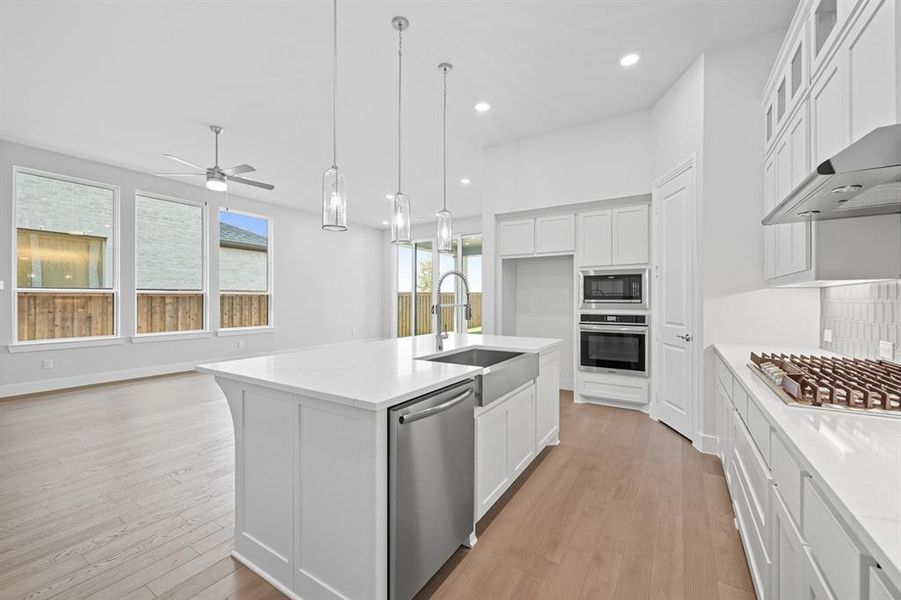 Kitchen featuring white cabinetry, appliances with stainless steel finishes, decorative light fixtures, recessed lighting, and a center island with sink Kitchen featuring white cabinetry, appliances with stainless steel finishes, decorative light fixtures, recessed lighting, and a center island with sink