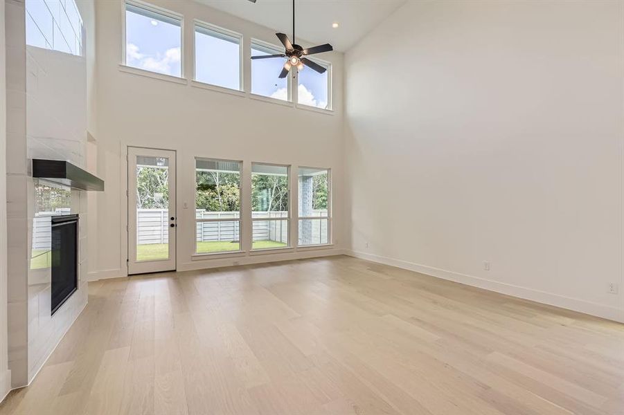 Unfurnished living room featuring a fireplace, light wood-style floors, a high ceiling, a ceiling fan, and baseboards Unfurnished living room featuring a fireplace, light wood-style floors, a high ceiling, a ceiling fan, and baseboards