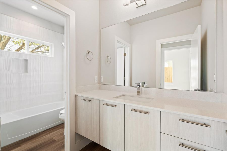 The shared full bath for the first-floor guest bedrooms, finished with a floating vanity, ample storage, and a clean tub-shower layout.
