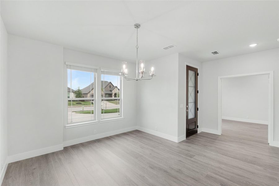 Empty dining room with chandelier, light wood floors, and double windows overlooking neighborhood