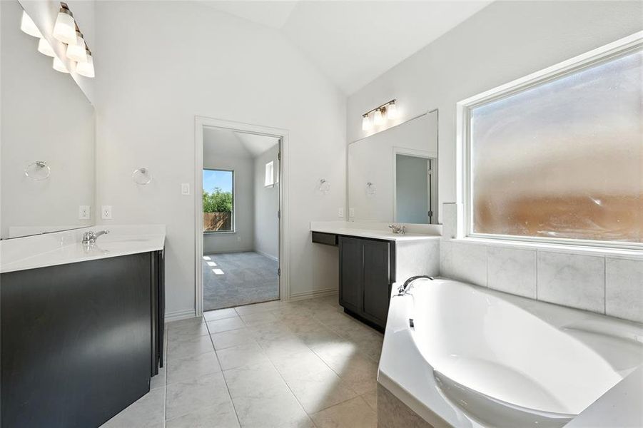 Full bath featuring two vanities, vaulted ceiling, and a bath