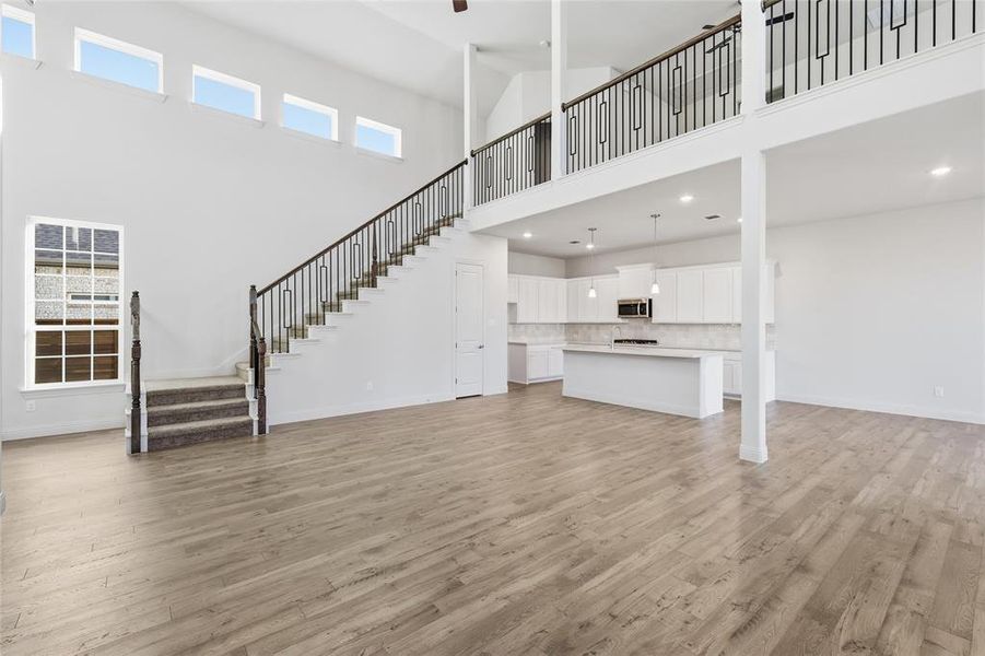 Unfurnished living room featuring stairs, light wood finished floors, and a towering ceiling