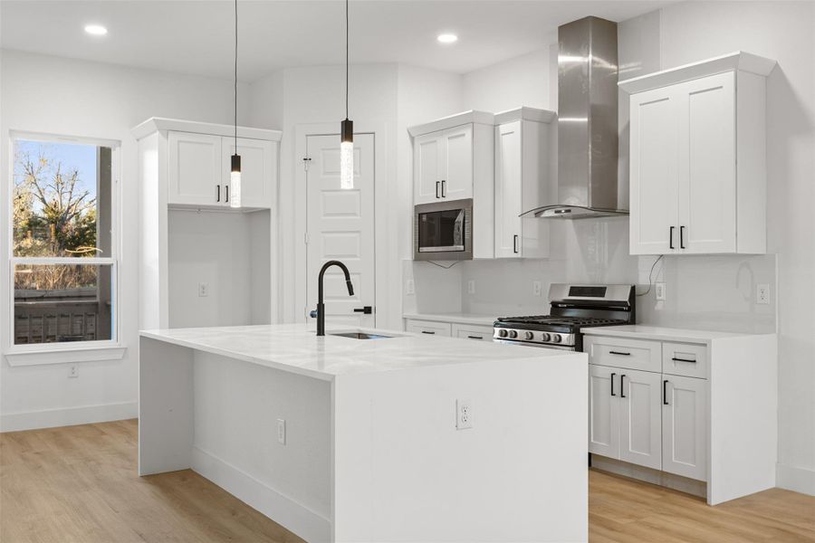 This modern kitchen features sleek white cabinetry, stainless steel appliances, and a central island with a built-in sink. The space is bright with natural light from the window and has elegant pendant lighting, ideal for cooking and entertaining.