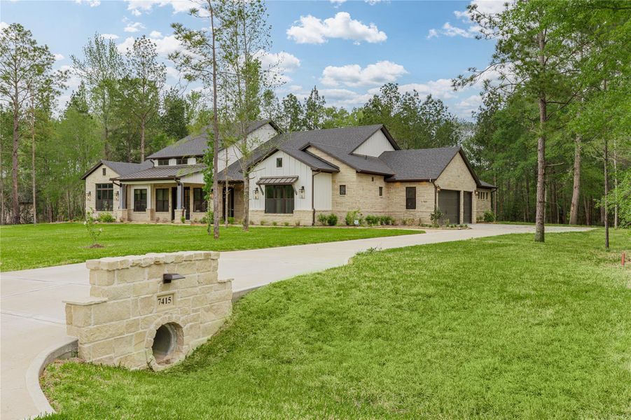 7415 Iron Valley Trail country living at its finest. Luxury living of 1.5 acres nestled in the tall pine trees. This front elevation shows tasteful design incorporating stone and metal accents with decorative lighting,