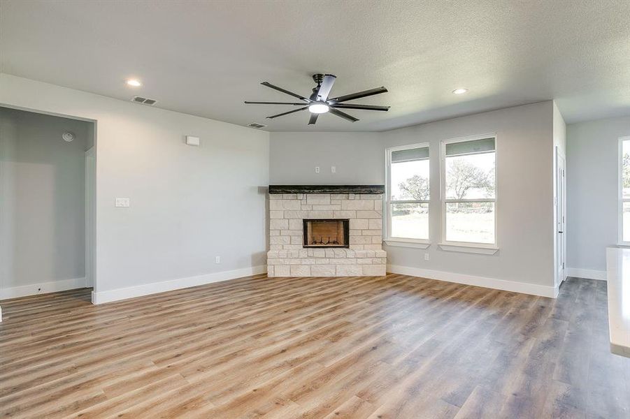 Unfurnished living room featuring light wood finished floors, ceiling fan, a fireplace, recessed lighting, and a textured ceiling