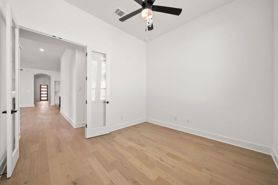 Unfurnished room with arched walkways, light wood-style floors, and a ceiling fan