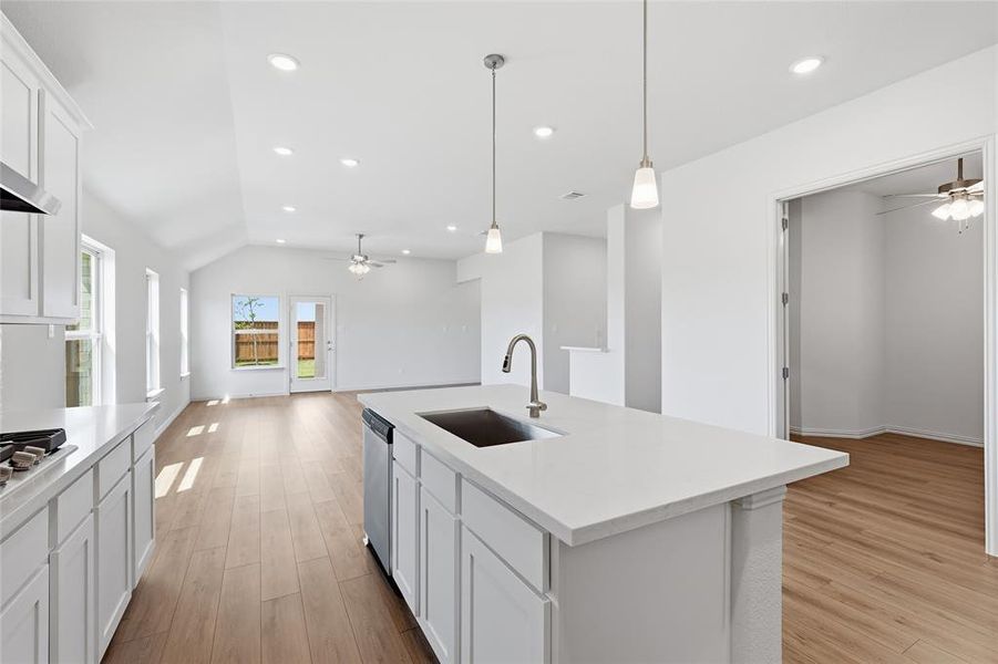 Kitchen with a ceiling fan, white cabinetry, pendant lighting, a center island with sink, and vaulted ceiling