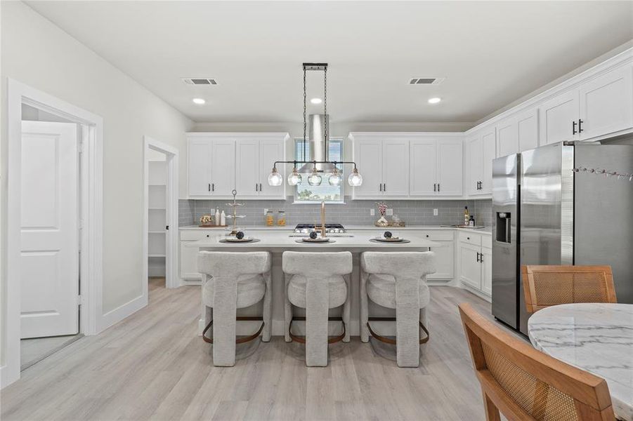 Kitchen with a breakfast bar area, stainless steel refrigerator with ice dispenser, backsplash, white cabinetry, and light wood-style flooring Kitchen with a breakfast bar area, stainless steel refrigerator with ice dispenser, backsplash, white cabinetry, and light wood-style flooring