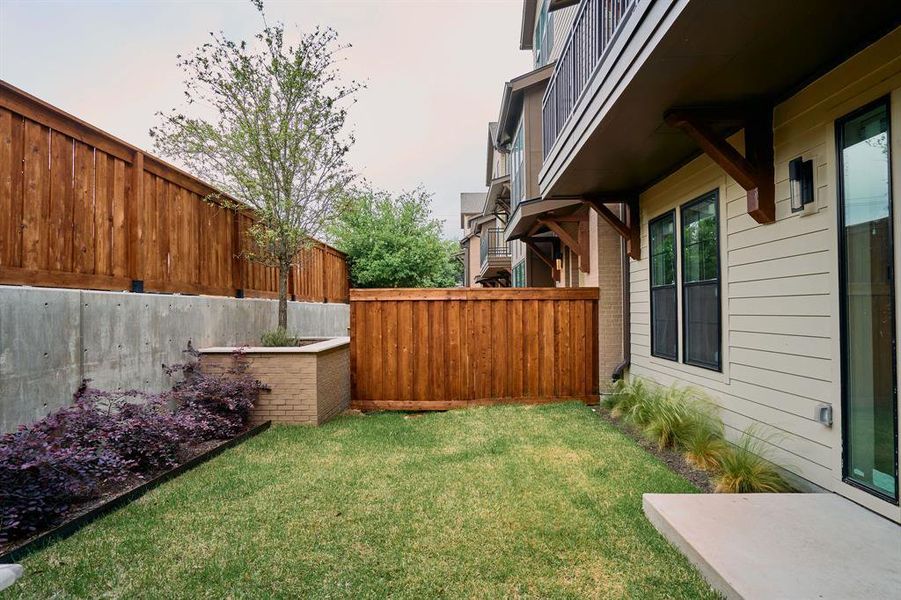 Private grassy yard with concrete patio, enclosed by stained wood fencing and a concrete retaining wall Private grassy yard with concrete patio, enclosed by stained wood fencing and a concrete retaining wall