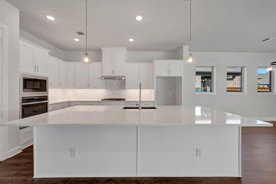 Kitchen with white cabinetry, a large island, dark wood-type flooring, and decorative light fixtures