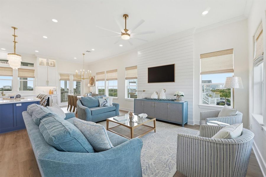 Large windows dressed with custom woven shades. Comfortable seating, and a wall-mounted Samsung Framed TV over shiplap wall. The space has light blue sofas, a modern ceiling fan, and access to a balcony with scenic views.