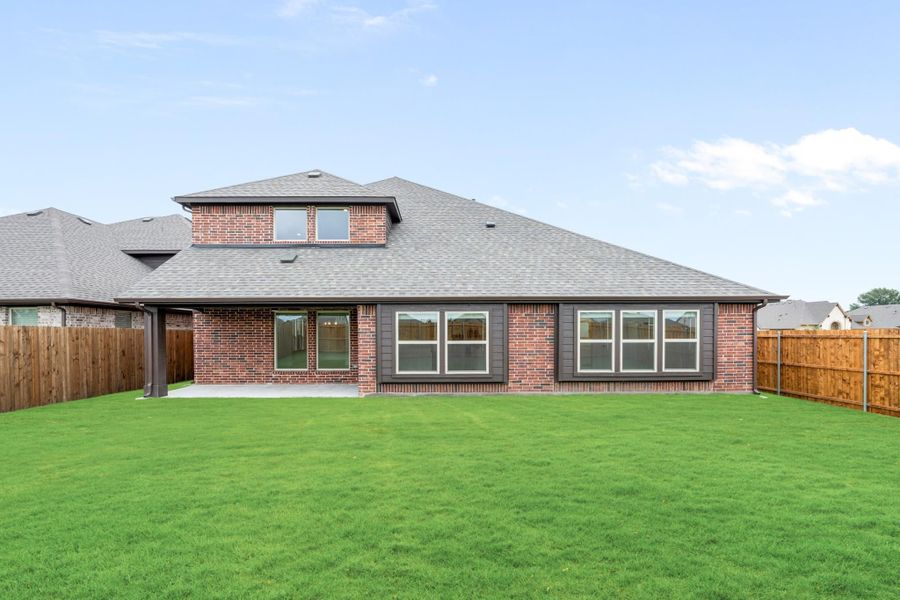 Rear view of two-story brick home with large windows, covered patio, and fenced backyard with green lawn Rear view of two-story brick home with large windows, covered patio, and fenced backyard with green lawn