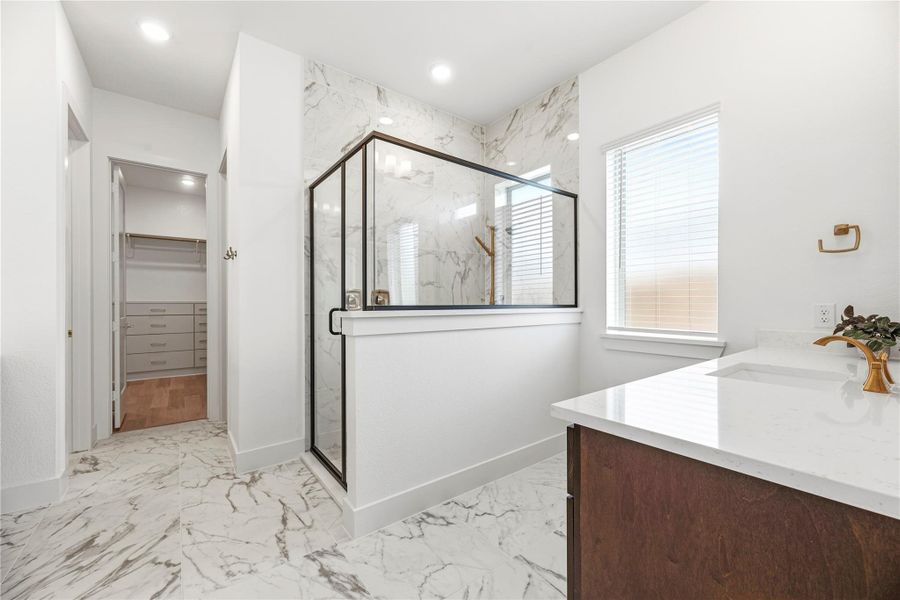 This refined Primary Bath is clad in high-end marble, featuring a seamless glass-enclosed shower, dual vanities, and a private, sophisticated design.