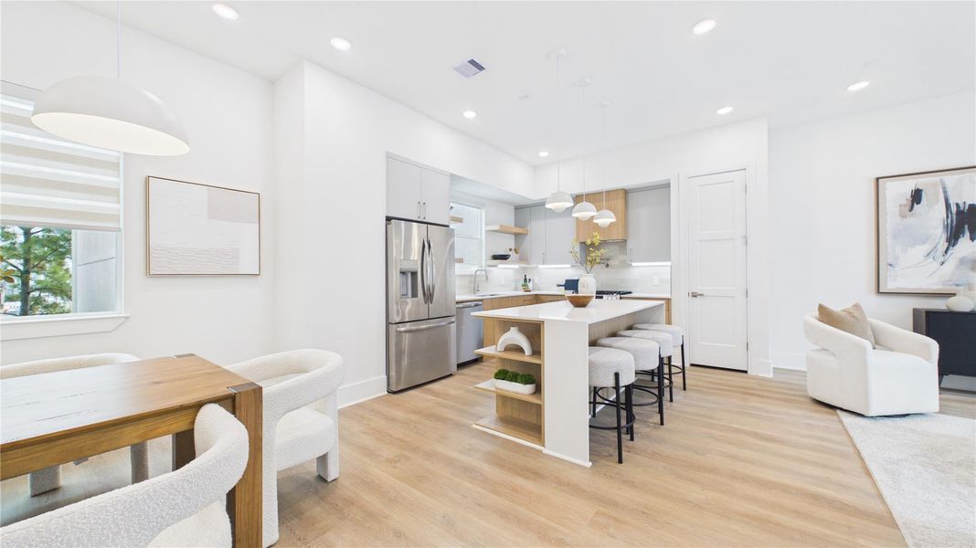 This photo showcases a modern, open-concept kitchen and dining area with sleek finishes. It features a large island with barstools, stainless steel appliances, and wood flooring. The space is bright, with ample natural light and contemporary decor.