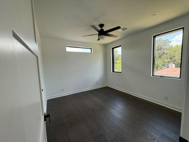 Spacious upstairs bedroom with abundant natural light and modern ceiling fan.