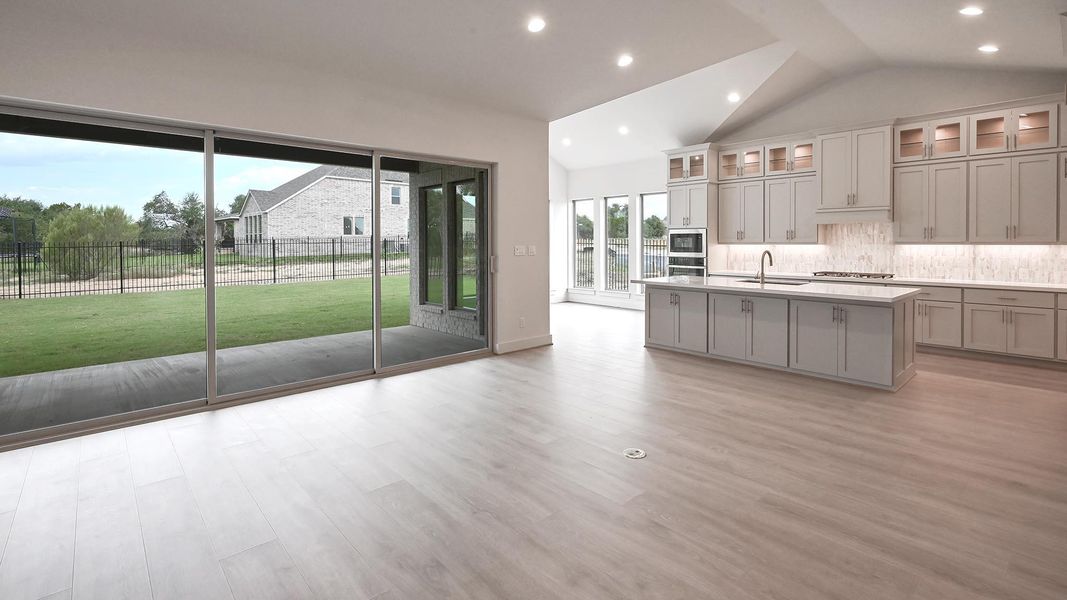 Kitchen featuring glass insert cabinets, light wood-style floors, recessed lighting, a kitchen island with sink, and vaulted ceiling