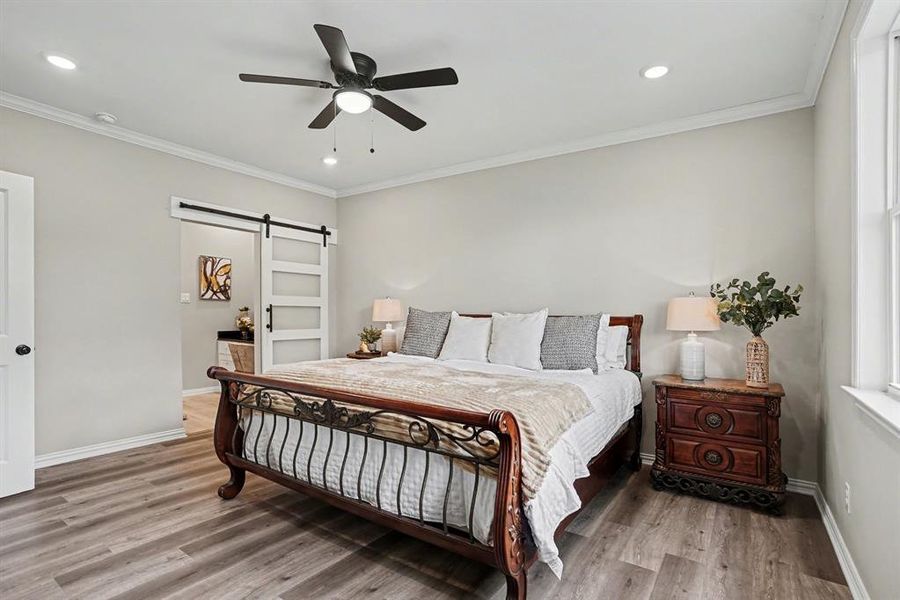 Bedroom featuring a barn door, crown molding, recessed lighting, light wood-style floors, and a ceiling fan
