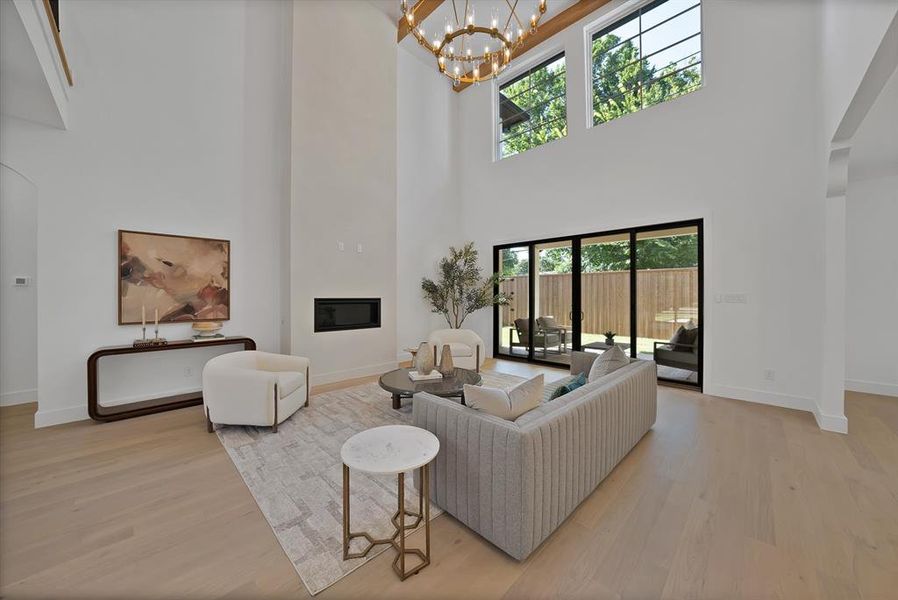 Two-story living area featuring wood-finish flooring, a linear fireplace, and high ceilings with an ornate chandelier