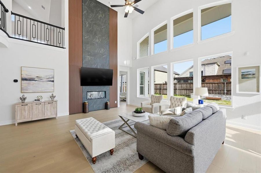 Two-story living room featuring a floor-to-ceiling fireplace with stone and wood paneling, wood-finish flooring, and a second-story balcony with metal railings