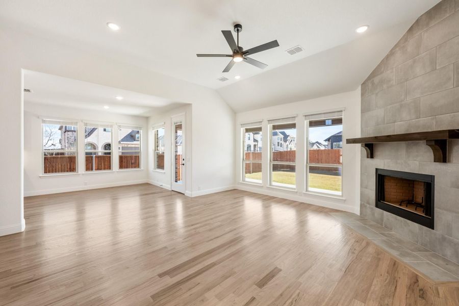 Open living room with hardwood floors, tile fireplace, ceiling fan, and large windows