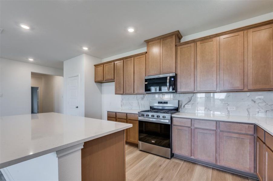 Kitchen featuring appliances with stainless steel finishes, light wood-style flooring, decorative backsplash, brown cabinets, and recessed lighting