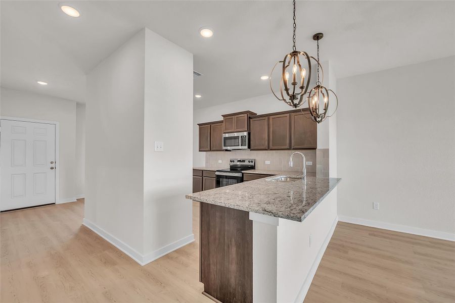 Kitchen featuring tasteful backsplash, stainless steel appliances, dark brown cabinetry, pendant lighting, and a chandelier