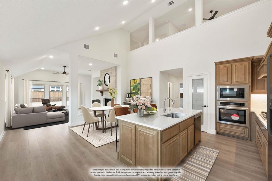 Open-concept kitchen with center island, wood cabinets, and stainless appliances flowing into dining and living areas with high ceilings Open-concept kitchen with center island, wood cabinets, and stainless appliances flowing into dining and living areas with high ceilings